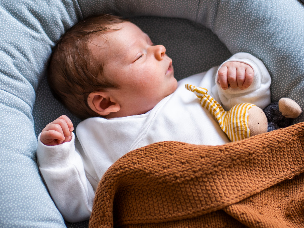 Baby schläft unter eine brauen Strickdecke.