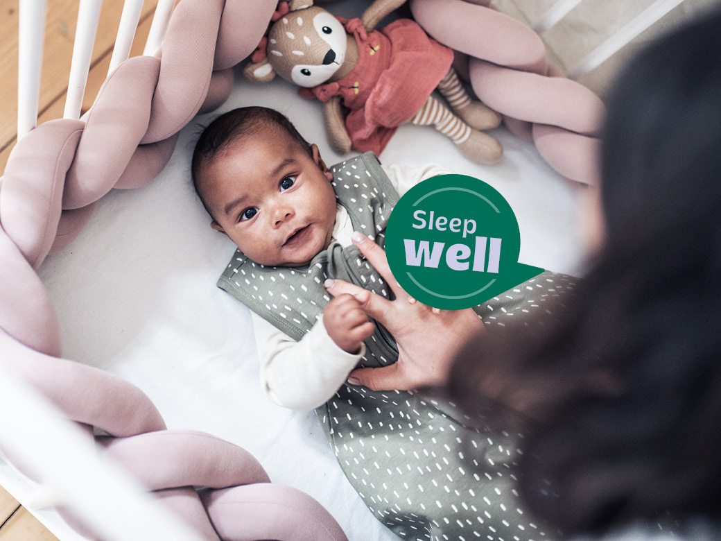 Baby in Schlafsack liegt im Bett