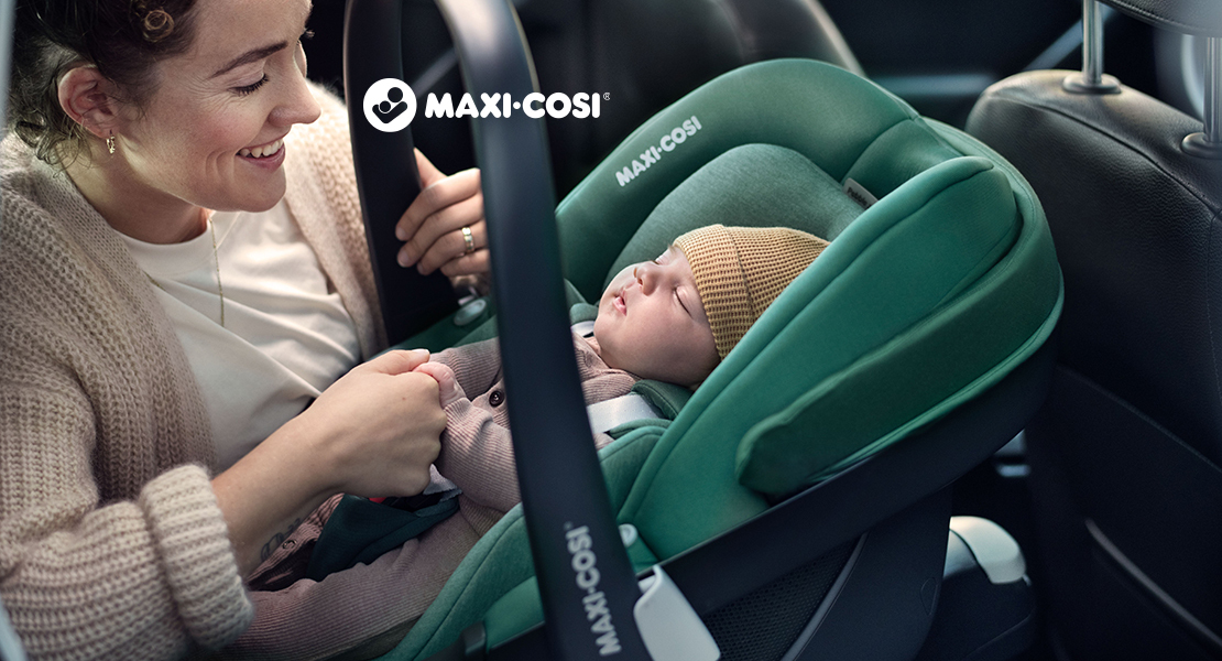 Eine frau, die ein baby auf einem autositz hält.