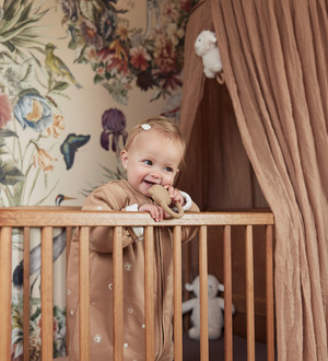 Ein Kleinkind steht in einem Gitterbett und kaut auf einem Beißring.