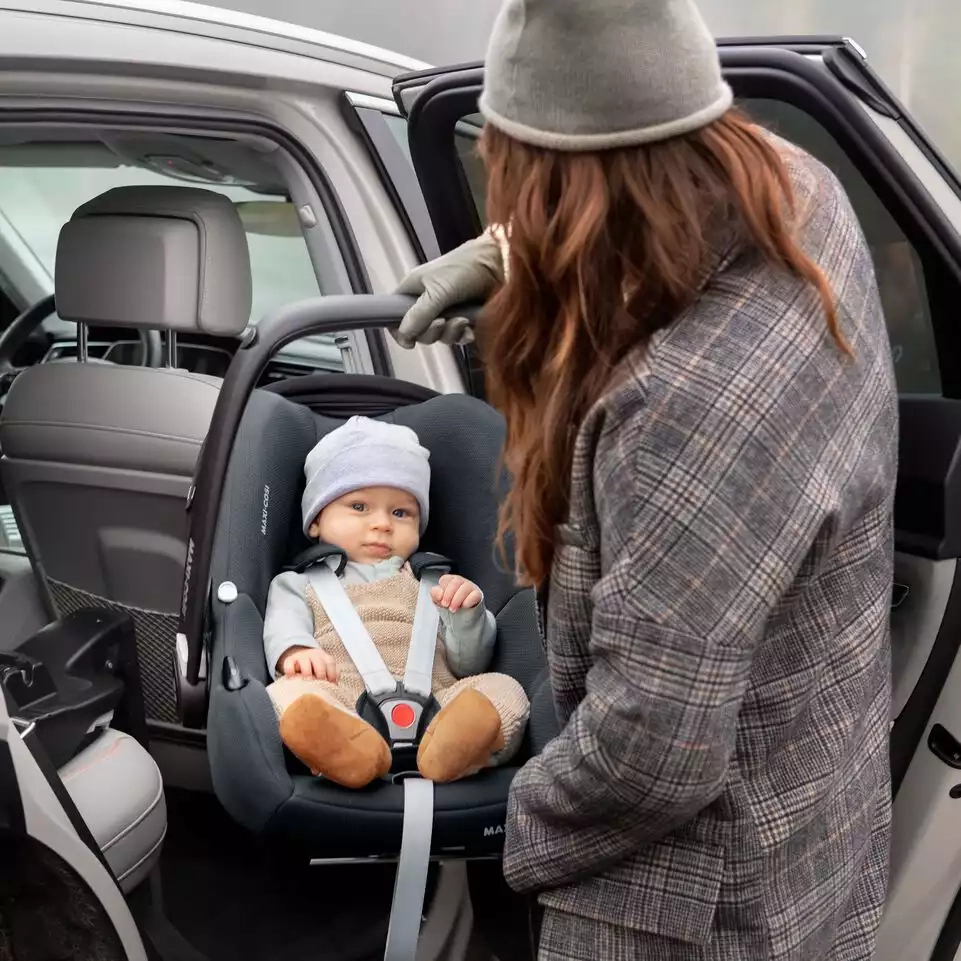 Eine frau, die ein baby auf einem autositz hält.