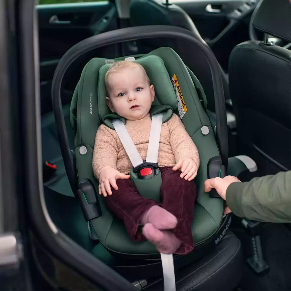 Eine frau, die ein baby auf einem autositz hält.