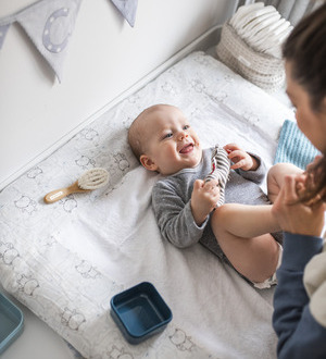 Ein lachendes Baby liegt auf einer weichen Wickelunterlage.